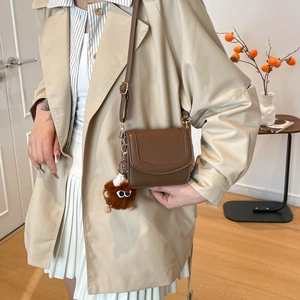 Schicke braune Leder-Umhängetasche mit Pompon-Anhänger in eleganter Seitenansicht