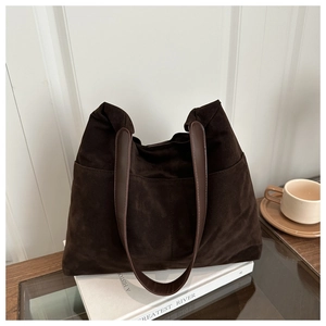 Gros plan d'un sac cabas en daim marron foncé avec poches latérales sur fond décoratif