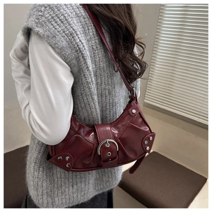 Detail of dark red crescent shoulder bag featuring silver buckle and rivet accents