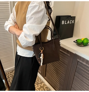 Detail of dark brown matte leather bucket bag featuring tri-color wooden bead tassel