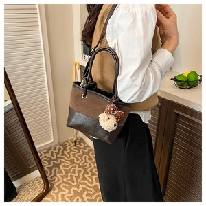 Detail of two-tone brown bucket bag with plush bear charm worn by a model
