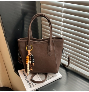Detail of dark brown matte leather bucket bag with wooden bead charm and embossed logo