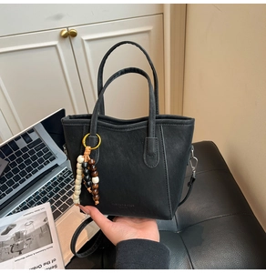 Detail of black matte leather tote bag featuring tricolor wood bead charm and long strap