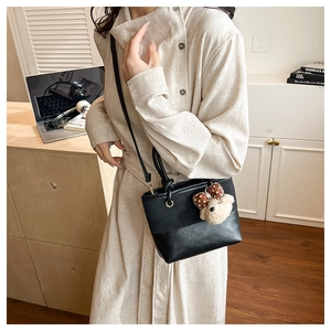 Detail of black leather bucket bag featuring a cute plush bear pendant on shoulder strap