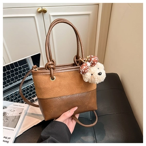 Detail of two-tone brown tote bag featuring suede texture and a cute bear charm