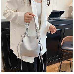 Detail of a silver metallic bucket bag featuring drawstring closure and chain handle