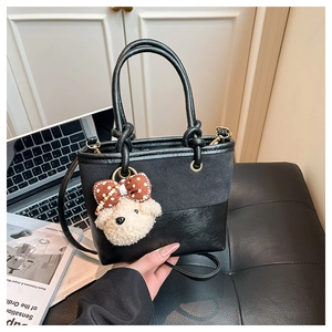 Detail of black crossbody bucket bag with cute plush bear charm on leather seat