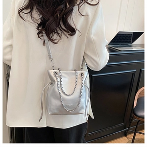 Detail of silver metallic bucket bag with drawstring closure and thick chain strap accessory