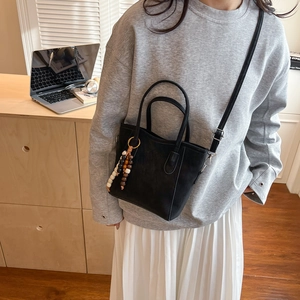 Chic black bucket bag with beaded charm accessory shown in a casual lifestyle setting