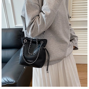 Close-up of black bucket bag with silver chain detail and drawstring closure shown on model