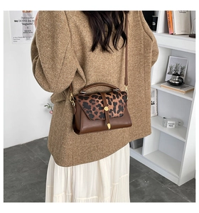 Detail of leopard print flap and gold metal hardware on a brown leather crossbody bag