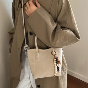 Minimalist beige crossbody bucket bag with wood bead tassel and adjustable strap on a model
