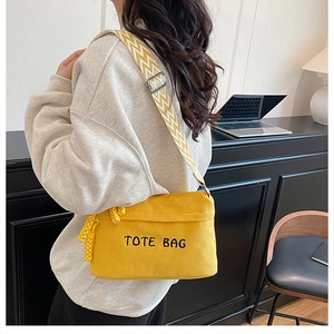 Model wearing yellow corduroy tote bag with TOTE BAG embroidery and zigzag strap