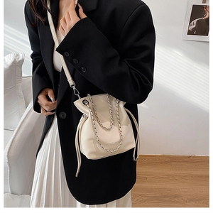 Detail of cream white bucket bag with drawstring closure and silver chain strap