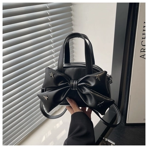 Detail of black leather crossbody bag with oversized bow and metal star rivets decor