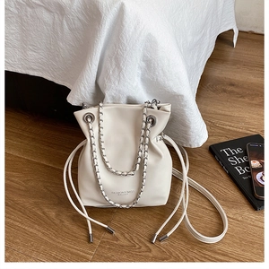 Detail of off-white drawstring bucket bag with silver chain strap on wooden floor
