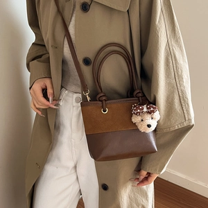 Brown leather tote bag with bear charm worn by a model in a khaki trench coat