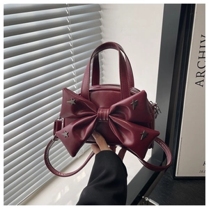 Detail of burgundy crossbody bag with oversized bow and silver star-shaped metal rivets
