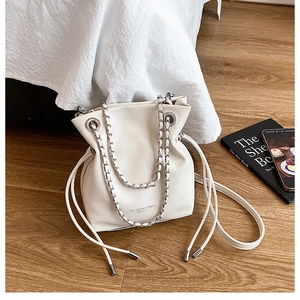 Detail of white drawstring bucket bag with silver chain strap on a wooden floor
