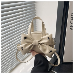 Detail of cream bow bucket bag with star rivets held by hand in a minimalist setting