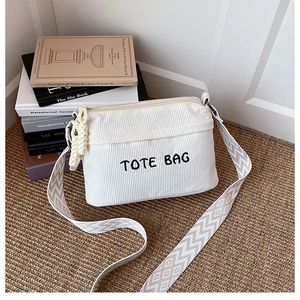 Detail of off-white corduroy tote bag featuring geometric strap and woven zipper pendant