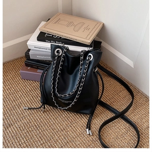Detail of black bucket bag showing matte leather texture and silver chain strap