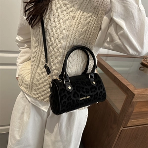 Fashionable black leopard print cylinder bag with gold hardware and shoulder strap