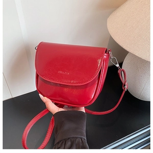 Detail of red saddle bag with embossed letters, leather strap and silver metal hooks