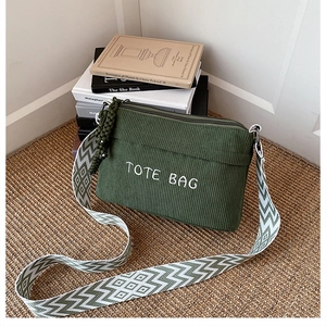 Detail of green corduroy crossbody bag with embroidered text and wide patterned strap