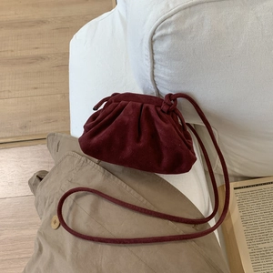 Détail macro du sac dumpling en daim bordeaux avec plis élégants et fine bandoulière