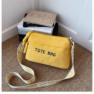 Detail of yellow corduroy crossbody bag with TOTE BAG embroidery and geometric strap
