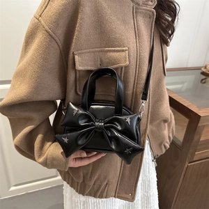 Stylish black mini crossbody bag with a large bow and silver star studs on a model