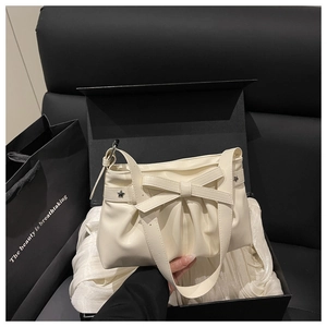Détail d'un sac à main blanc crème avec nœud décoratif, rivets en étoile et plis élégants