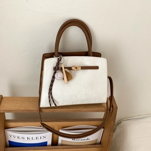 Detail of white and brown contrast tote bag featuring gold lock and baseball charm