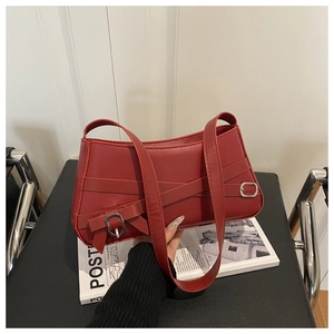 Detail of burgundy shoulder bag with cross straps and silver buckles on black chair