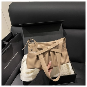 Détail d'un sac à bandoulière beige plissé avec nœud papillon et boucles étoiles en coffret