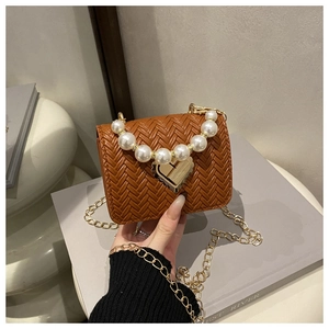 Detail of woven brown handbag featuring a large pearl handle and gold heart clasp