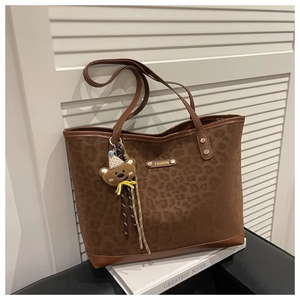 Détail du sac cabas léopard avec porte-clés ours et logo doré sur fond de livre