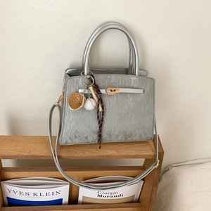 Detail of silver textured tote bag with metal twist lock and baseball themed pendants