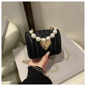 Detail view of woven black crossbody bag with large pearl accents and gold heart clasp