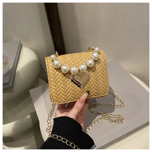 Detail of woven crossbody bag featuring large pearl handle and heart-shaped metal lock