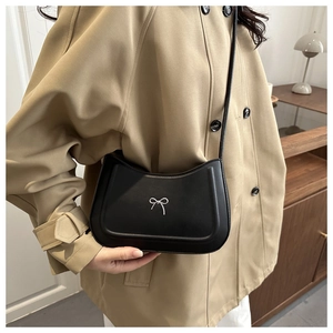Dettaglio borsa a tracolla a mezzaluna nera con fiocco argento su trench beige