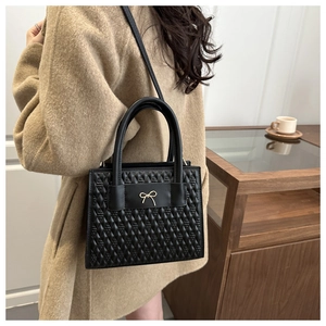Sac bandoulière matelassé noir avec boucle nœud dorée présenté dans un décor chic