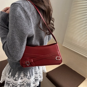 Minimalist red leather baguette bag with silver buckle and cross straps on women's shoulder