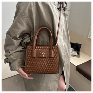 Detail view of brown quilted PU leather texture and gold bow buckle on small handbag