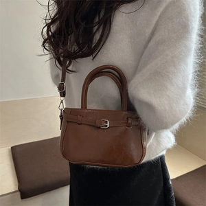 Sac à main en cuir marron avec boucle argentée porté par un mannequin en pull blanc doux