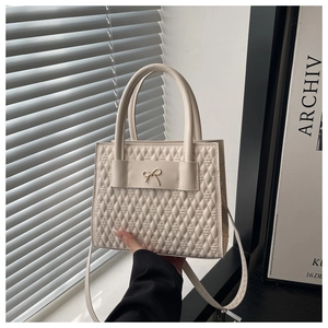 Gros plan du sac carré crème matelassé avec fermoir nœud doré et textures fines