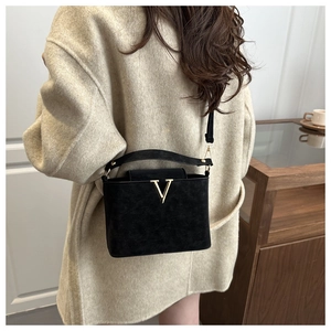 Détail d'un sac carré en cuir noir mat avec logo V doré et une bandoulière ajustable