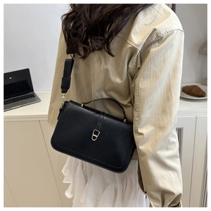 Detail of black crossbody bag with gold D-ring buckle on white pleated skirt