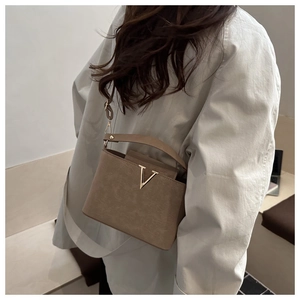 Petit sac carré marron avec boucle en V dorée porté par un mannequin pour le style